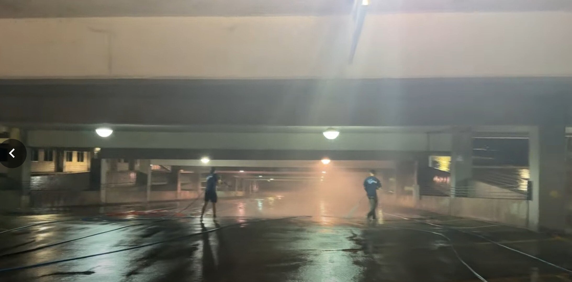 KC Splash technician pressure washing K-State parking garage floor with Park directional signs overhead — overnight operation