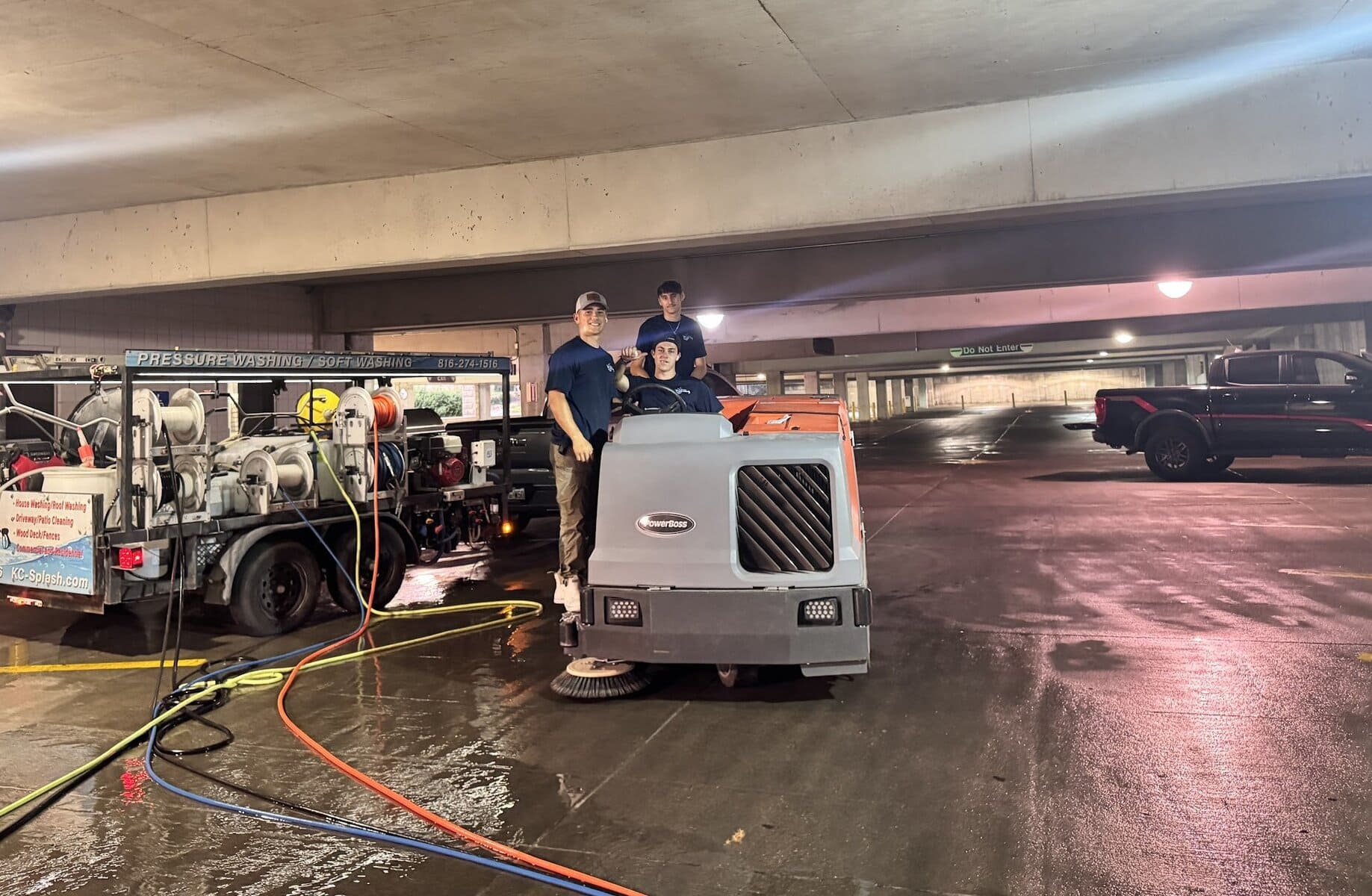 Two KC Splash crew members on open level of K-State garage at night with steam and city lights visible