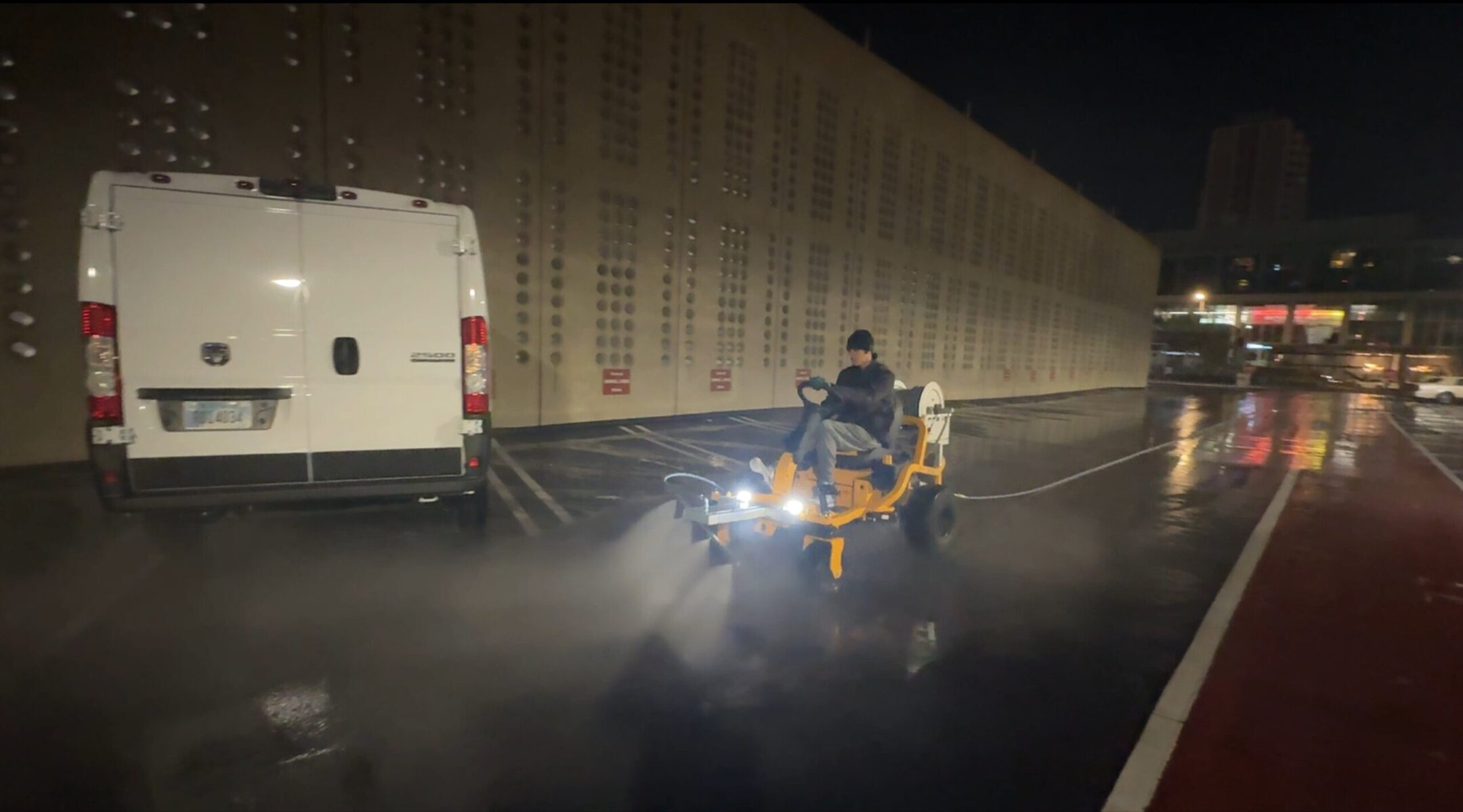 The Beast ride-on surface cleaner on open rooftop deck at night with city skyline visible