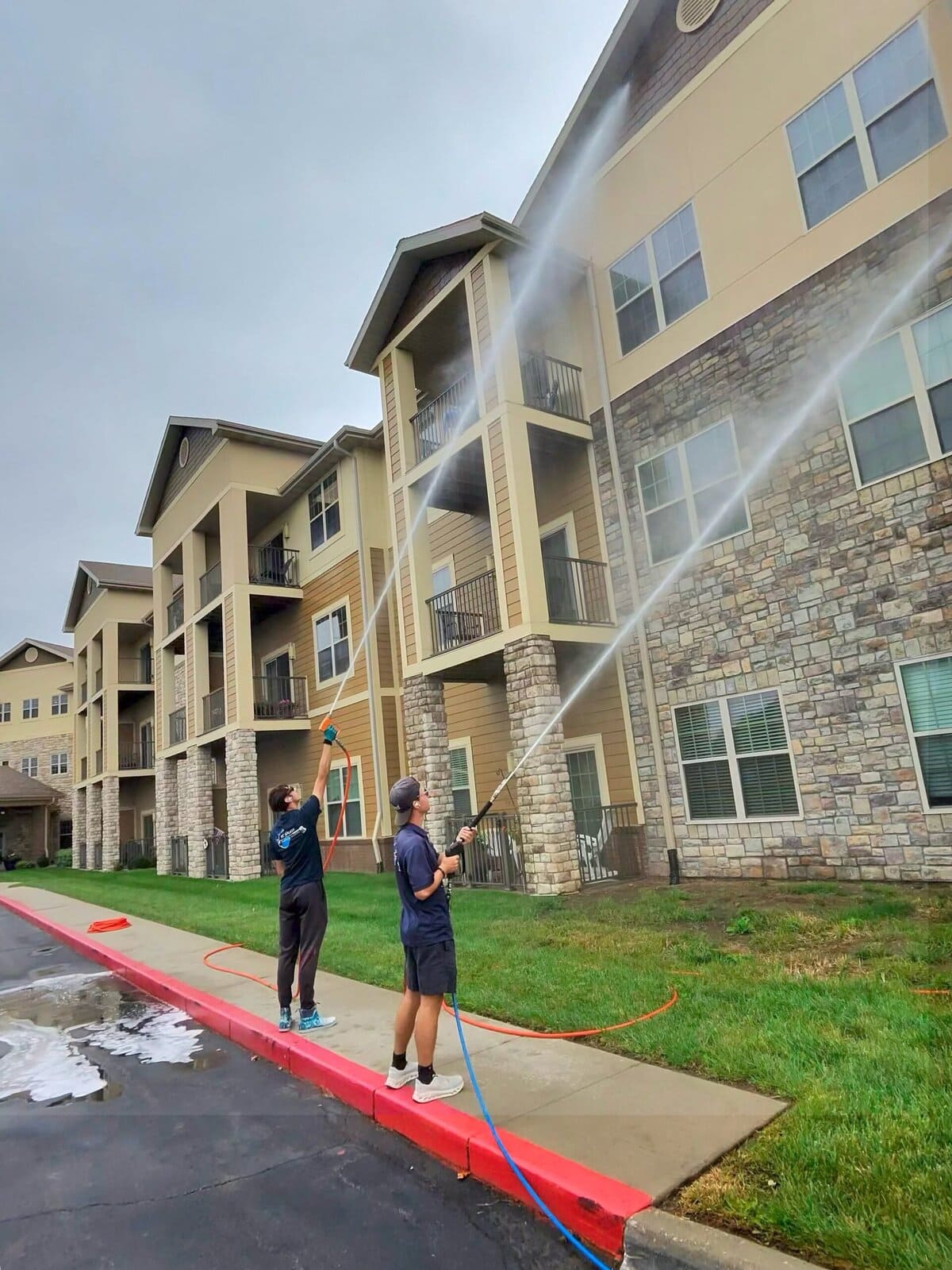 KC Splash crew member reaching 3 stories to wash senior living building exterior — steam visible