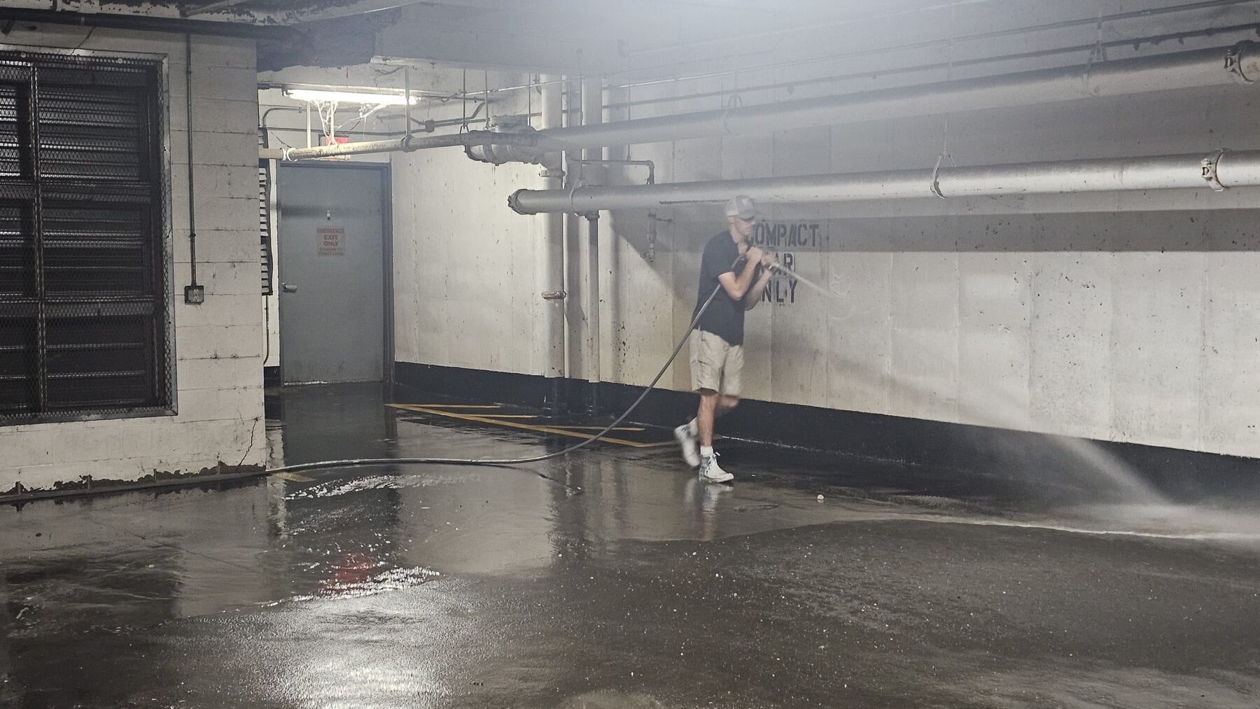 Crew member hand pressure washing edge work inside the Lightwell parking garage